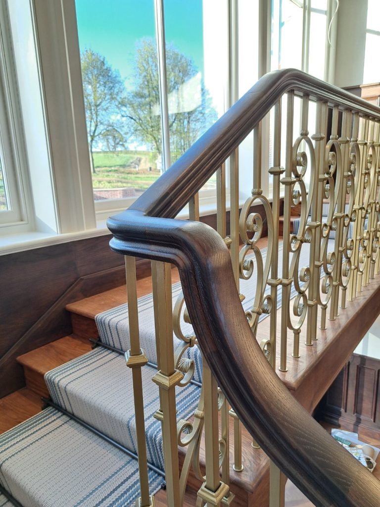 Dark-stained solid oak handrail with swan-neck over gold scrolled balusters